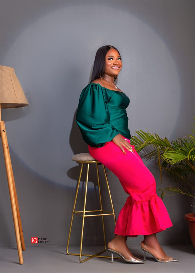 Dominica Izunobi seated on a stool in a studio, smiling